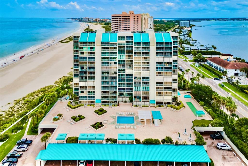 An aerial view shows a tall beachfront condominium building with a pool and parking area — 1380 GULF BOULEVARD UNIT 805, CLEARWATER, FL