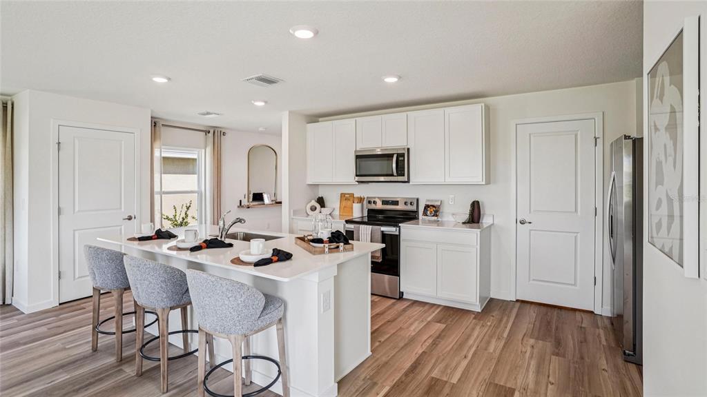 A kitchen features white cabinets, a central island with three stools, and light wood flooring — 2118 NE 33RD LANE, OCALA, FL