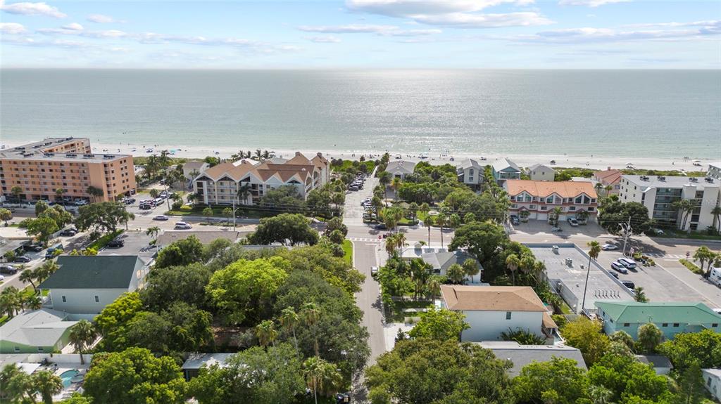 An aerial view shows a coastal neighborhood with multi-story buildings, lush trees, and a beach — 104 12TH AVENUE, INDIAN ROCKS BEACH, FL