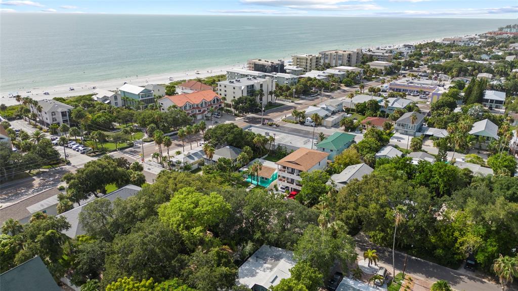 An aerial view shows a coastal neighborhood with houses, palm trees, and a sandy beach — 104 12TH AVENUE, INDIAN ROCKS BEACH, FL