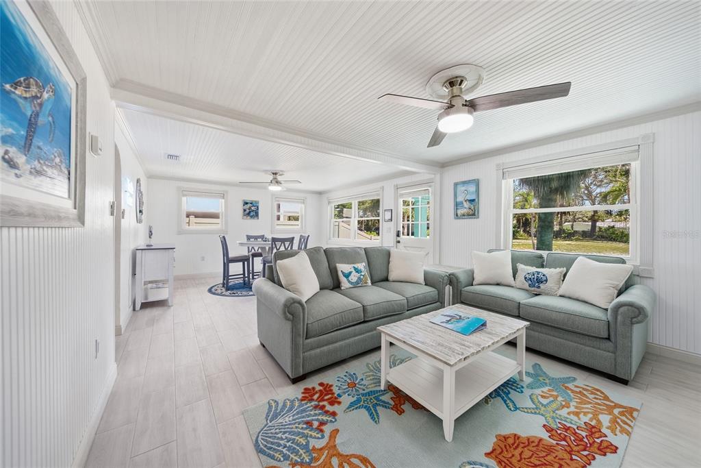 A living room features light wood floors, beadboard ceilings, two teal sofas, and coastal decor — 104 12TH AVENUE, INDIAN ROCKS BEACH, FL