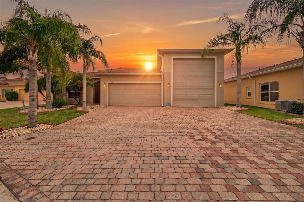A house exterior with a paved driveway, two garage doors, and palm trees at sunset — 4120 LIMERICK DRIVE, LAKE WALES, FL