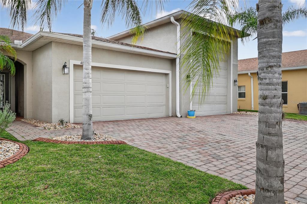A beige house exterior features a two-car garage, a paver driveway, and palm trees — 4120 LIMERICK DRIVE, LAKE WALES, FL