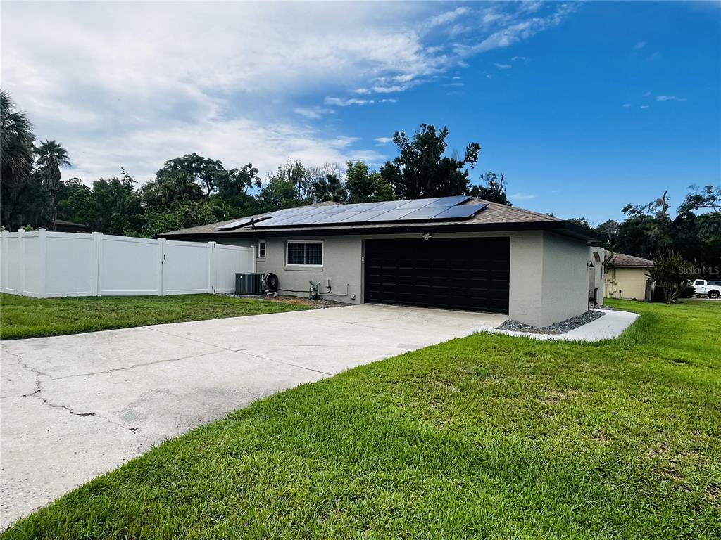 A single-story house with a black garage door, solar panels on the roof, and white fencing — 3370 SE 31ST TERRACE, OCALA, FL