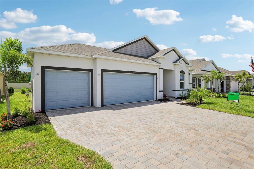 A single-story house with a three-car garage and a paved driveway under a blue sky — 25129 CALUSA DRIVE, PUNTA GORDA, FL