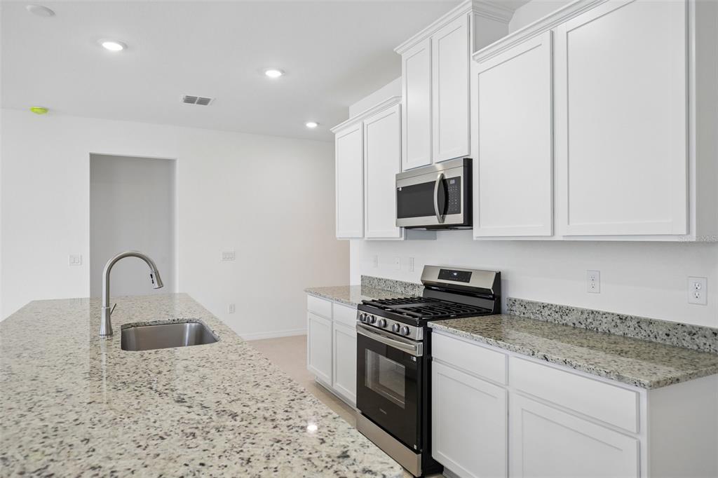 A kitchen features white cabinets, granite countertops, a stainless steel oven, and a center island — 25129 CALUSA DRIVE, PUNTA GORDA, FL