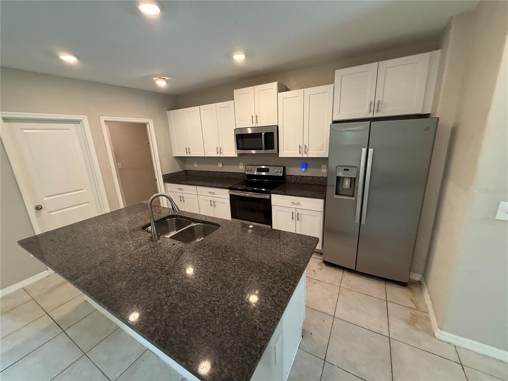A kitchen features white cabinets, granite countertops, a center island, and stainless steel appliances — 1752 COLDING DRIVE, RUSKIN, FL
