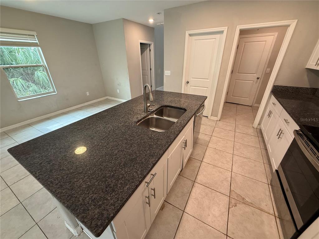 A kitchen features a dark granite island with a sink, white cabinets, and tile flooring — 1752 COLDING DRIVE, RUSKIN, FL