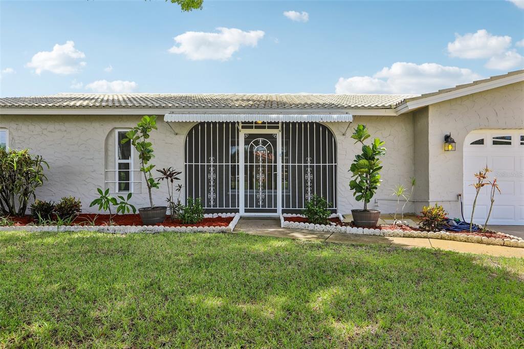 A single-story house exterior features a white stucco facade, a security-barred entryway, and a garage — 13178 88TH AVENUE N, SEMINOLE, FL