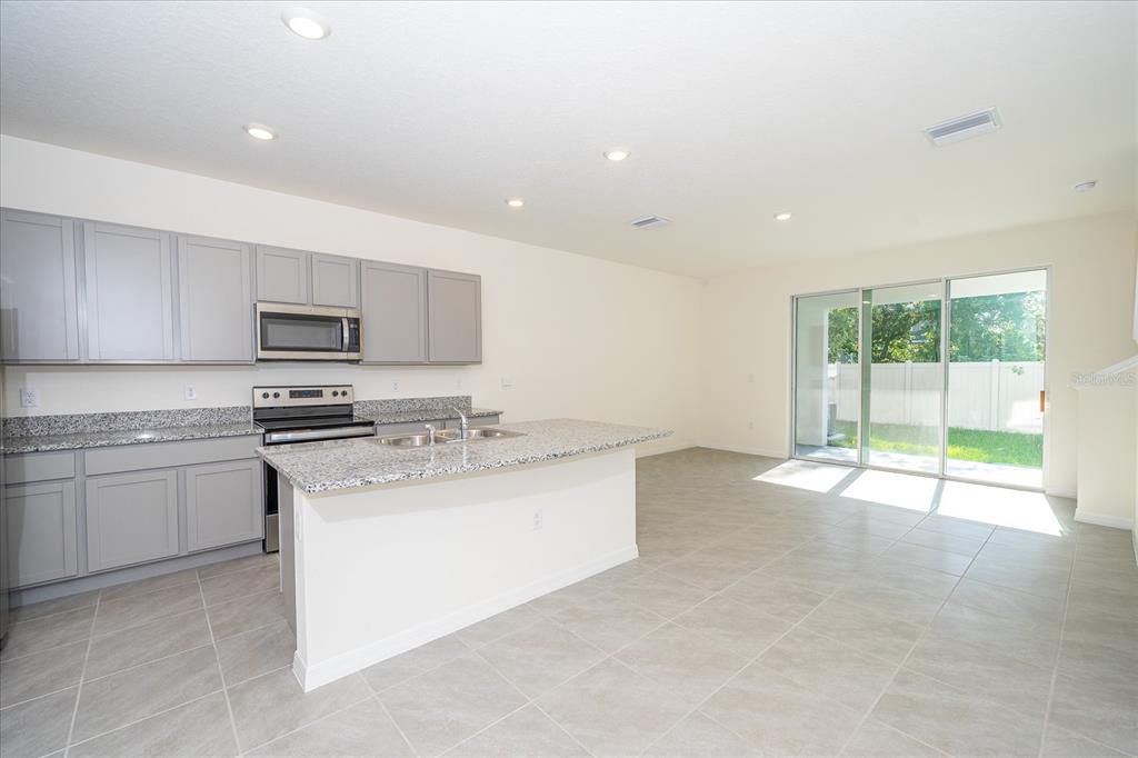 A kitchen with gray cabinets, granite countertops, and an island opens to a tiled living area — 16642 MAUDE DRIVE, WIMAUMA, FL