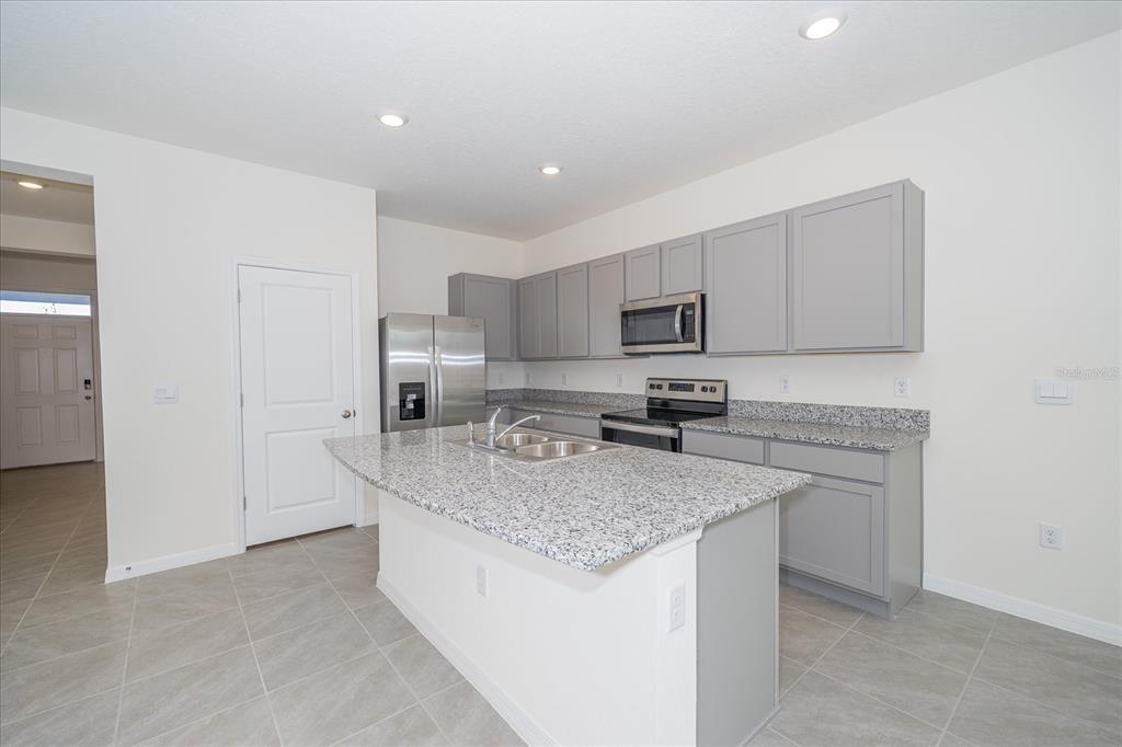 A kitchen features gray cabinets, granite countertops, a center island, and stainless steel appliances — 16642 MAUDE DRIVE, WIMAUMA, FL