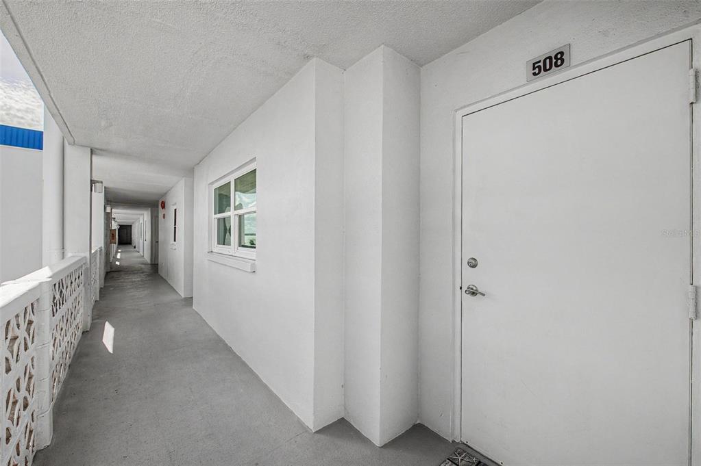 An exterior view of a building hallway featuring a white door labeled 508 — 7 ELGIN PLACE UNIT 508, DUNEDIN, FL