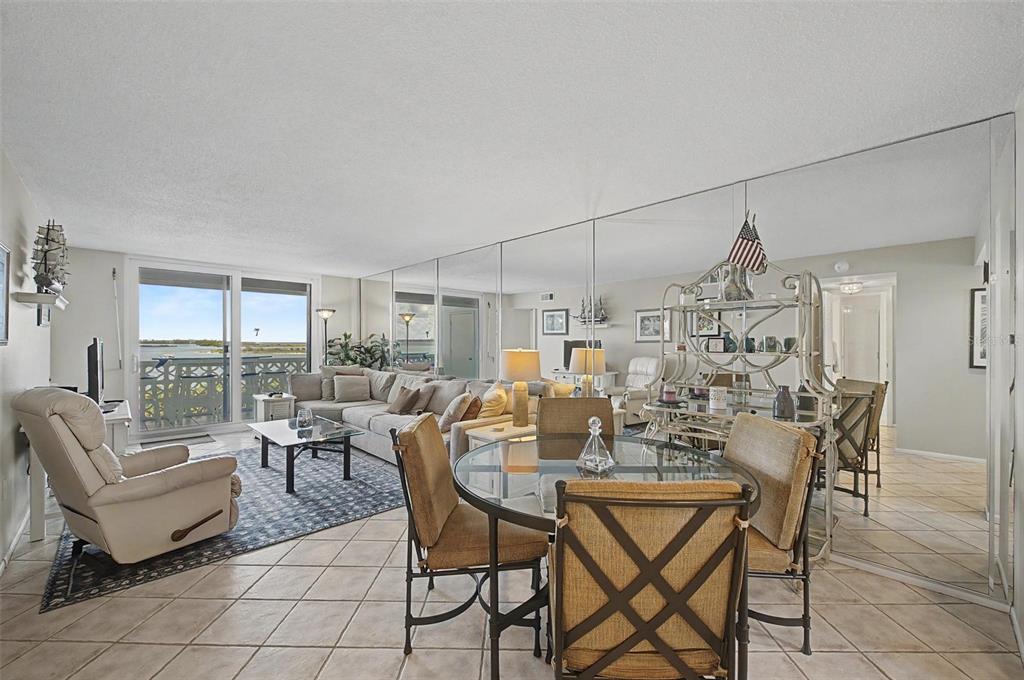 A living and dining area features tiled floors, mirrored walls, and a view of water — 7 ELGIN PLACE UNIT 508, DUNEDIN, FL