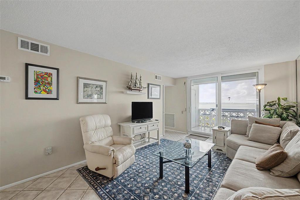A living room features a beige recliner, a sectional sofa, a glass coffee table, and balcony access — 7 ELGIN PLACE UNIT 508, DUNEDIN, FL