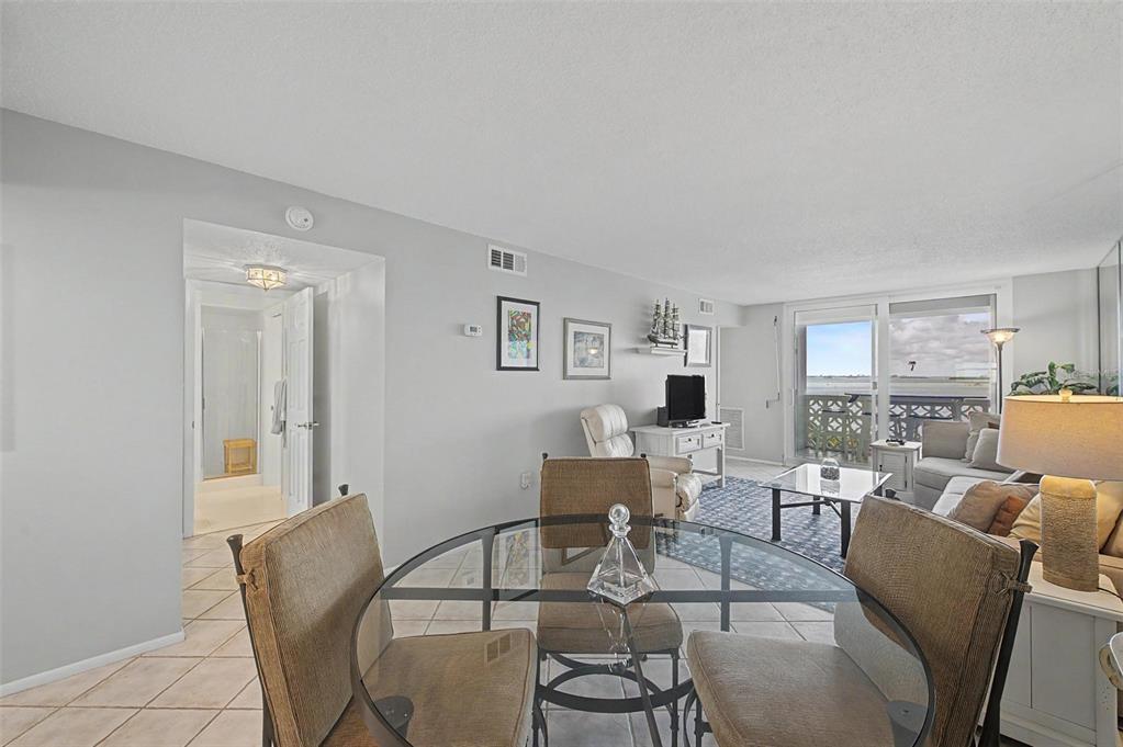 A dining area with a glass table overlooks a living room with a water view — 7 ELGIN PLACE UNIT 508, DUNEDIN, FL