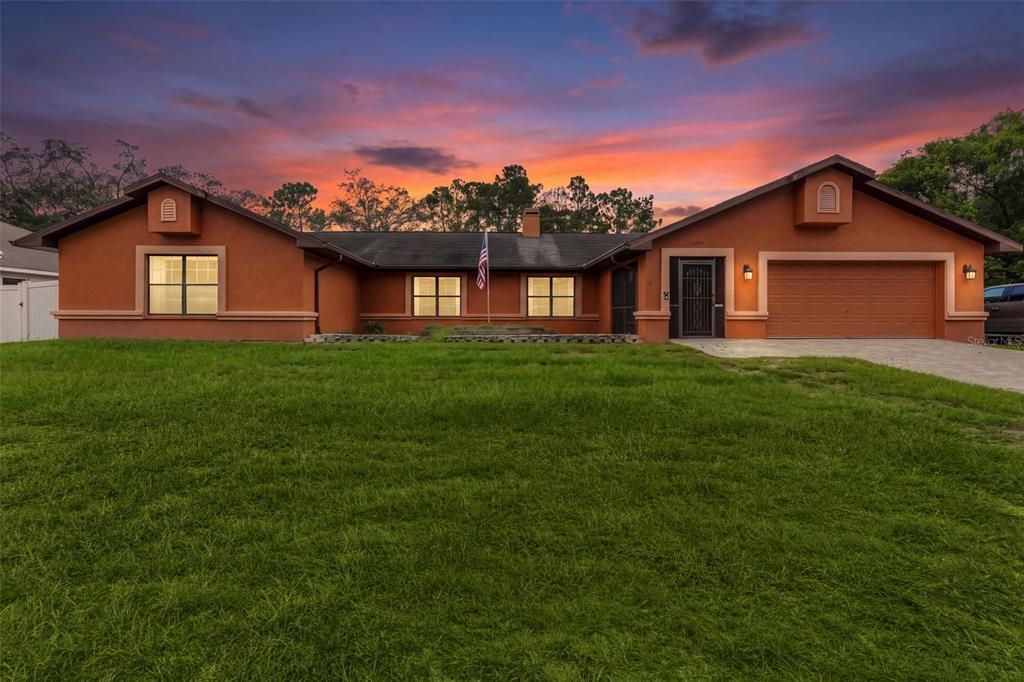 A single-story house with a terracotta exterior, a two-car garage, and a large front lawn — 4289 CASTLE AVENUE, SPRING HILL, FL