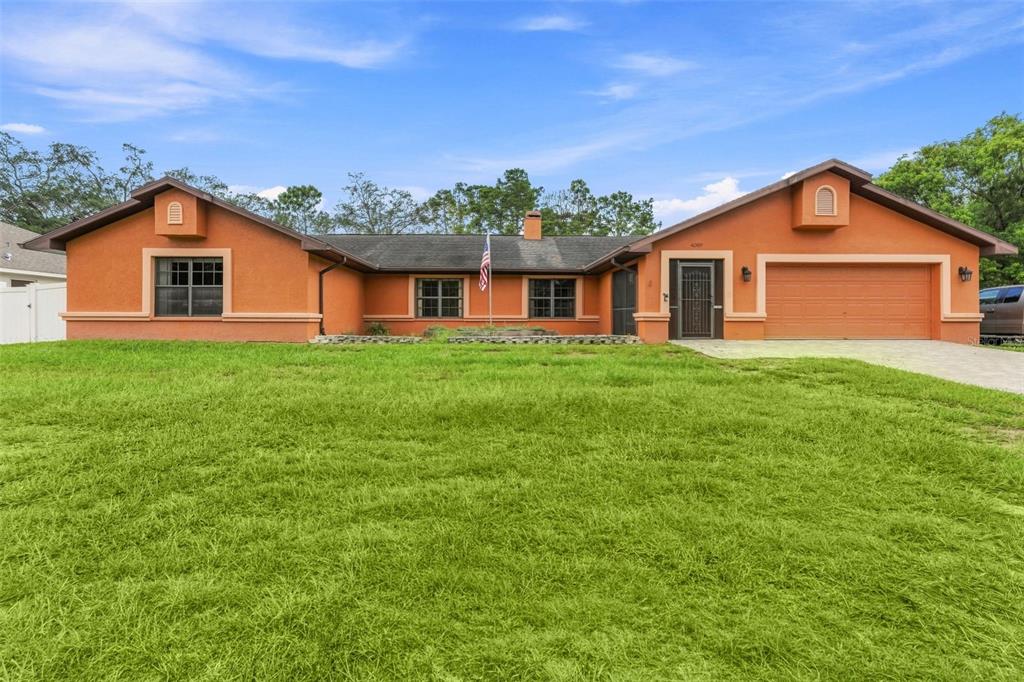 A single-story orange stucco house with a two-car garage and a large front lawn — 4289 CASTLE AVENUE, SPRING HILL, FL