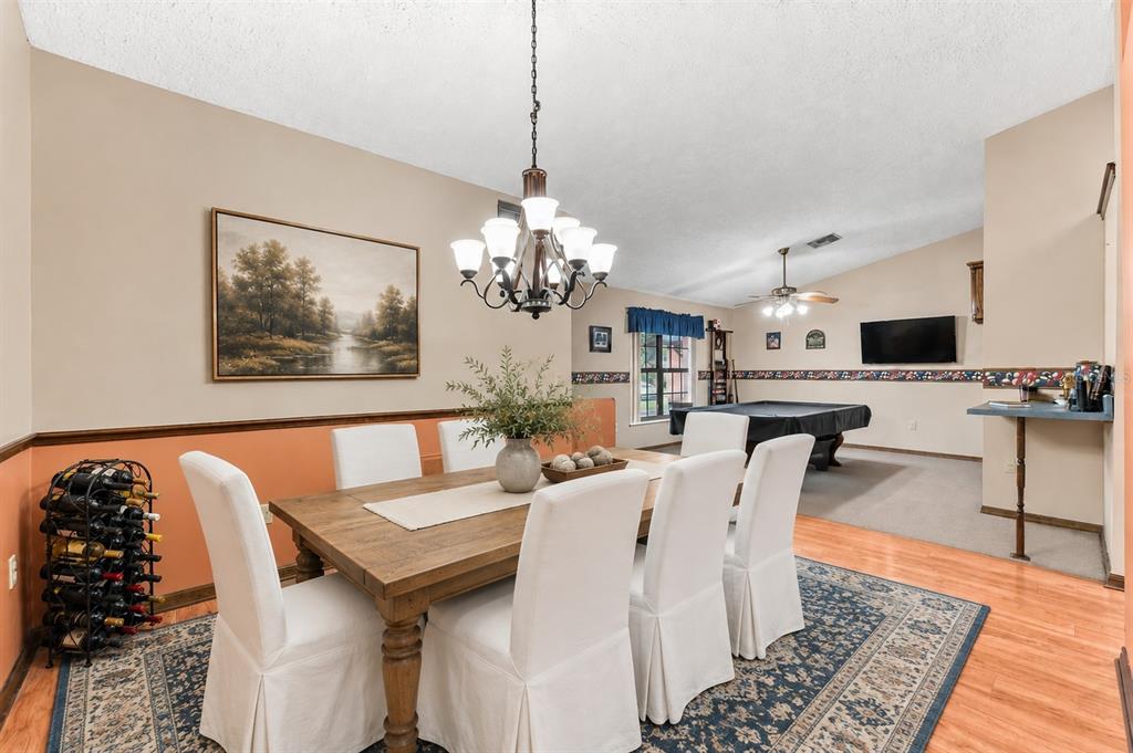 A dining area with a wooden table and chairs sits adjacent to a carpeted game room — 4289 CASTLE AVENUE, SPRING HILL, FL
