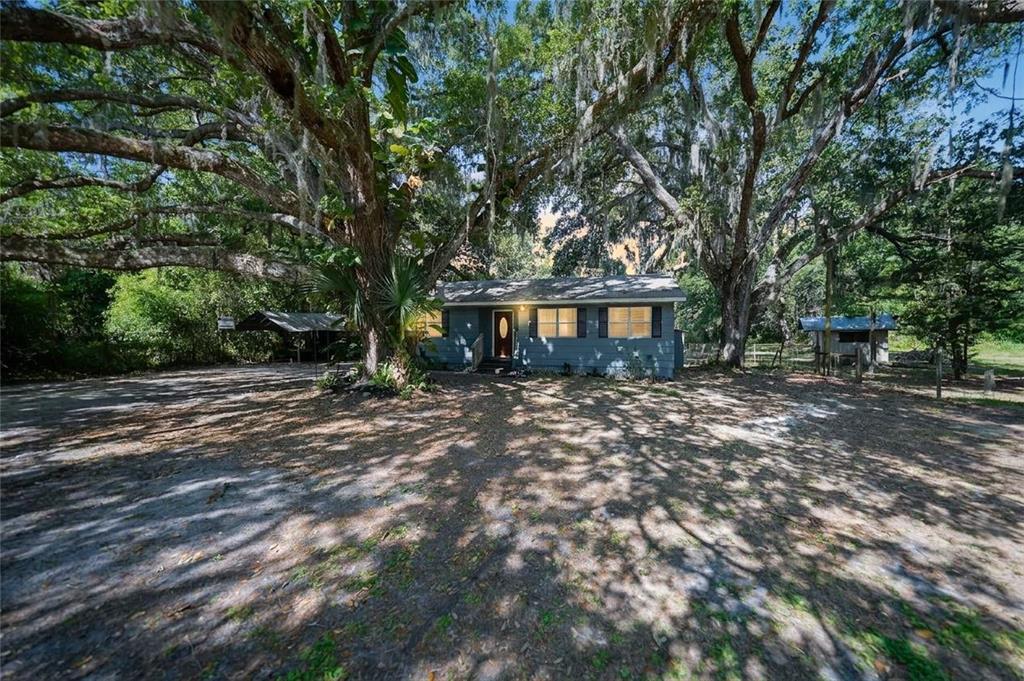 A blue single-story house sits on a dirt lot shaded by large, moss-covered oak trees — 2403 SE POINTER AVENUE, ARCADIA, FL