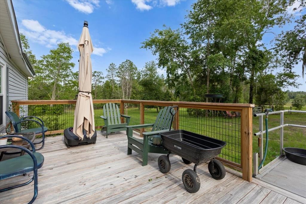 A wooden deck features patio chairs, a closed umbrella, and a black garden cart — 7220 NE 24TH LOOP, HIGH SPRINGS, FL