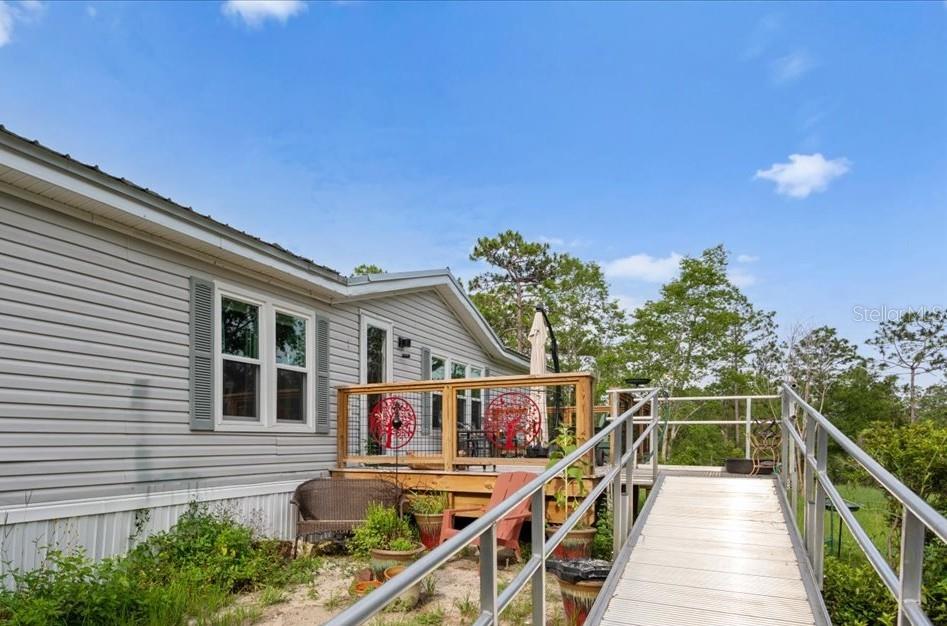 A light gray mobile home features a wooden deck with metal railings and an access ramp — 7220 NE 24TH LOOP, HIGH SPRINGS, FL