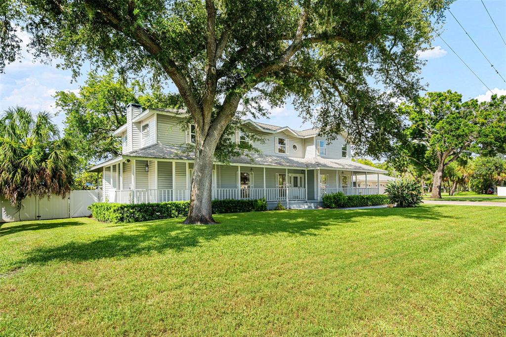 A two-story light gray house with a wrap-around porch sits on a large grassy lawn — 2002 8TH STREET W, PALMETTO, FL