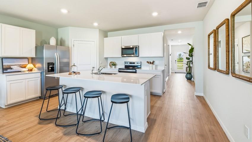 A kitchen features white cabinets, a central island with bar stools, and light wood flooring — 2027 VANDALIA PLACE, PARRISH, FL