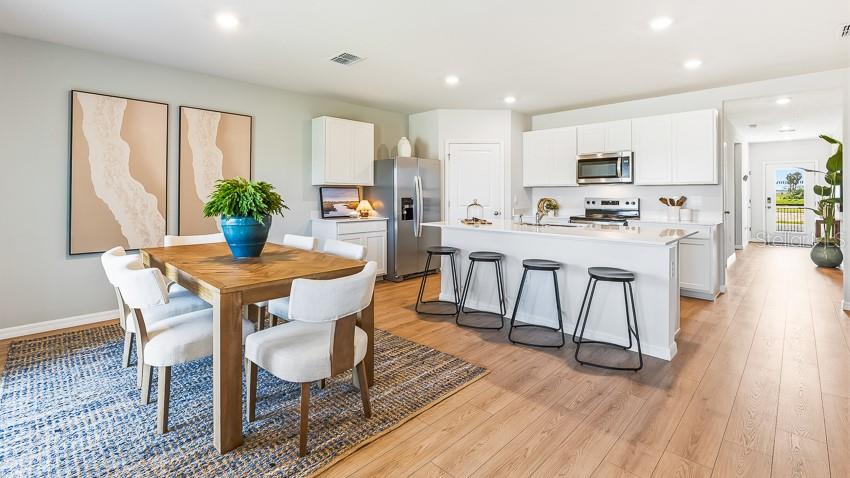 A modern kitchen with white cabinetry and an island opens to a dining area — 2027 VANDALIA PLACE, PARRISH, FL