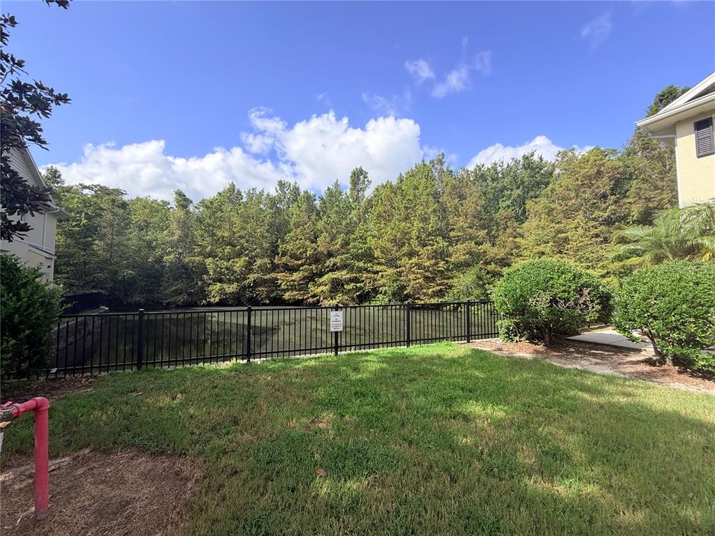 A grassy backyard area features a black metal fence overlooking a pond and dense trees — 10703 REGENT SQUARE DRIVE UNIT 1801, ORLANDO, FL