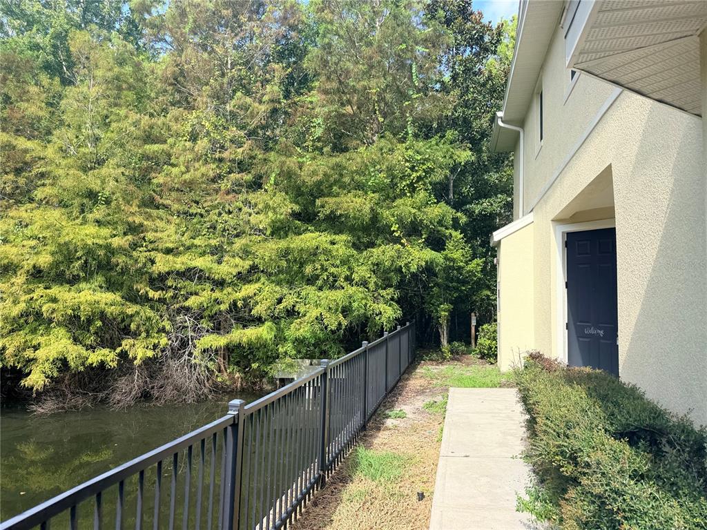 A concrete walkway runs alongside a house exterior next to a black metal fence and pond — 10703 REGENT SQUARE DRIVE UNIT 1801, ORLANDO, FL