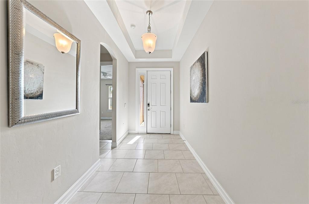 A bright entryway features light tile flooring, a tray ceiling with a pendant light, and mirrors — 719 HEATHER LAKE AVENUE, CAPE CORAL, FL