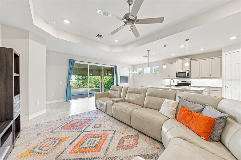 A spacious living room with a large sectional sofa, tile floors, and an open kitchen — 719 HEATHER LAKE AVENUE, CAPE CORAL, FL