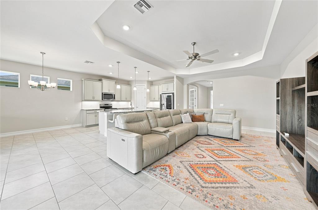 A spacious open-concept living room and kitchen featuring light tile floors and a tray ceiling — 719 HEATHER LAKE AVENUE, CAPE CORAL, FL