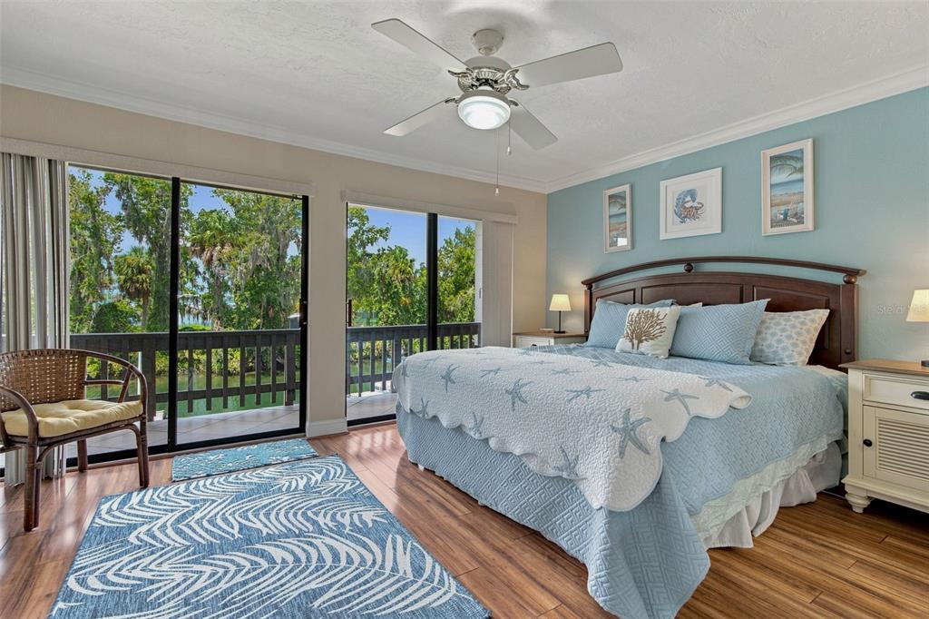 A bedroom with a king bed, blue coastal decor, wood floors, and a balcony view — 65 BEACH LANE UNIT N, CRYSTAL RIVER, FL