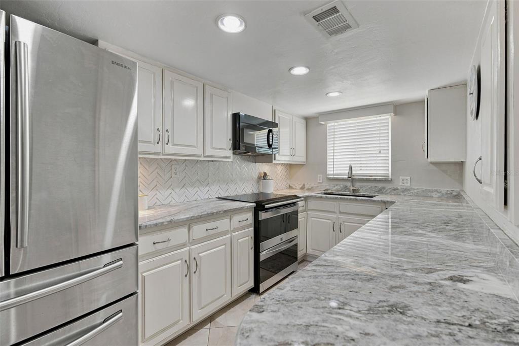 A kitchen with white cabinets, stainless steel appliances, and gray-veined marble countertops — 65 BEACH LANE UNIT N, CRYSTAL RIVER, FL