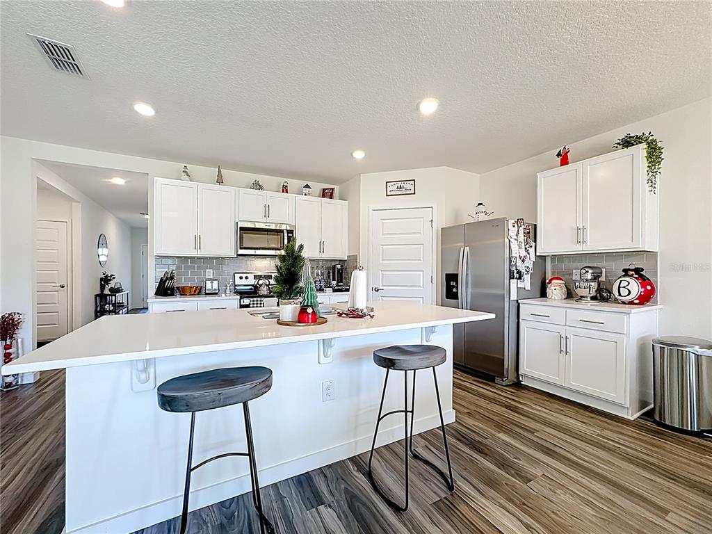 A modern kitchen features white cabinets, a large island with bar stools, and stainless steel appliances — 348 TALISI LOOP, ST CLOUD, FL