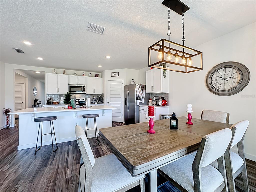 A kitchen with white cabinets and an island opens to a dining area with seating — 348 TALISI LOOP, ST CLOUD, FL