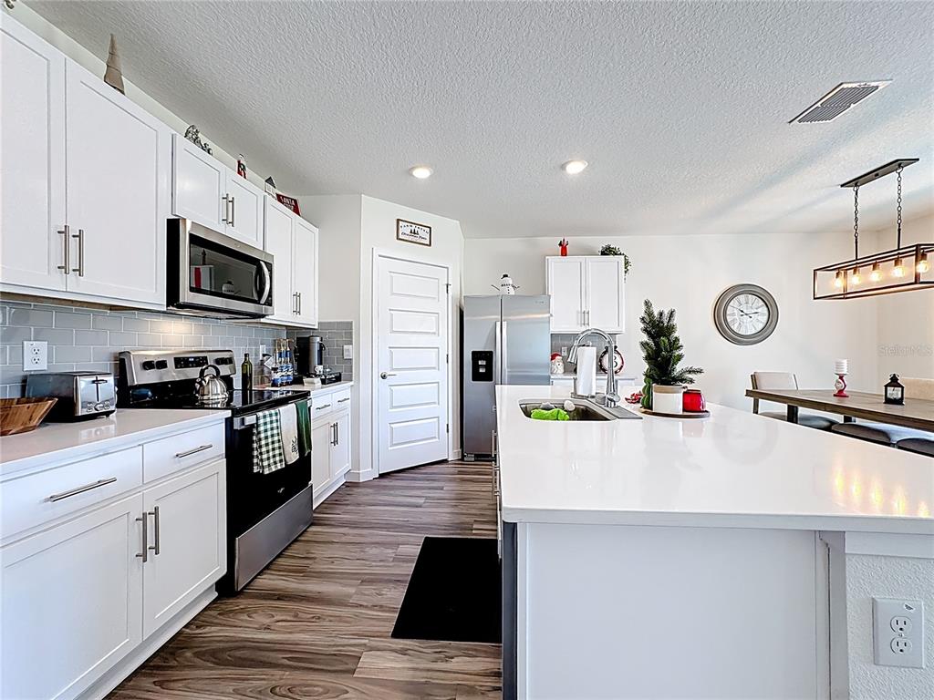 A modern kitchen features white cabinetry, stainless steel appliances, a large island, and wood-look flooring — 348 TALISI LOOP, ST CLOUD, FL