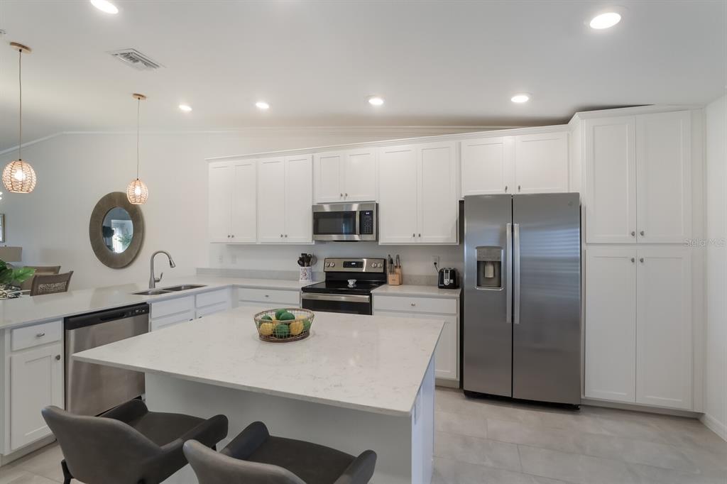 A modern kitchen features white cabinetry, stainless steel appliances, a quartz island, and pendant lighting — 5721 PALMER CIRCLE UNIT 201, BRADENTON, FL