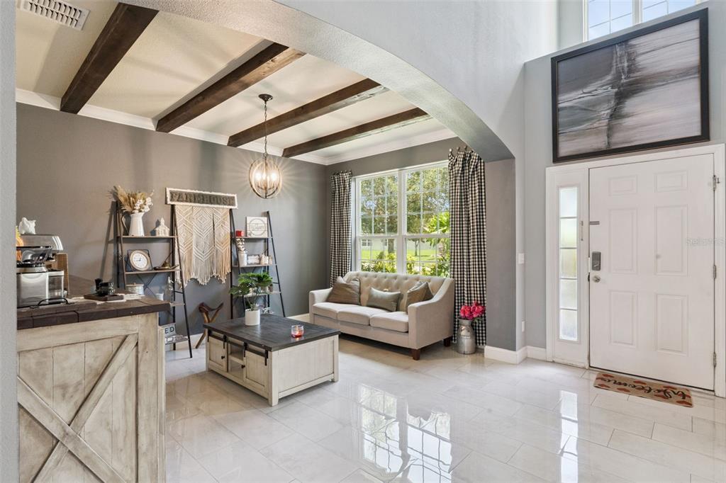 A living room features a tufted sofa, wooden ceiling beams, and a white front door — 4750 CYPRESS FOREST LANE, ST CLOUD, FL