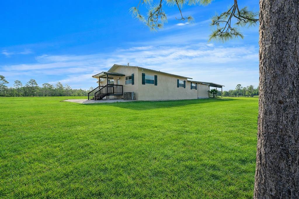 A single-story house with a small porch sits in a large, open grassy field — 12451 NE 20TH STREET, WILLISTON, FL