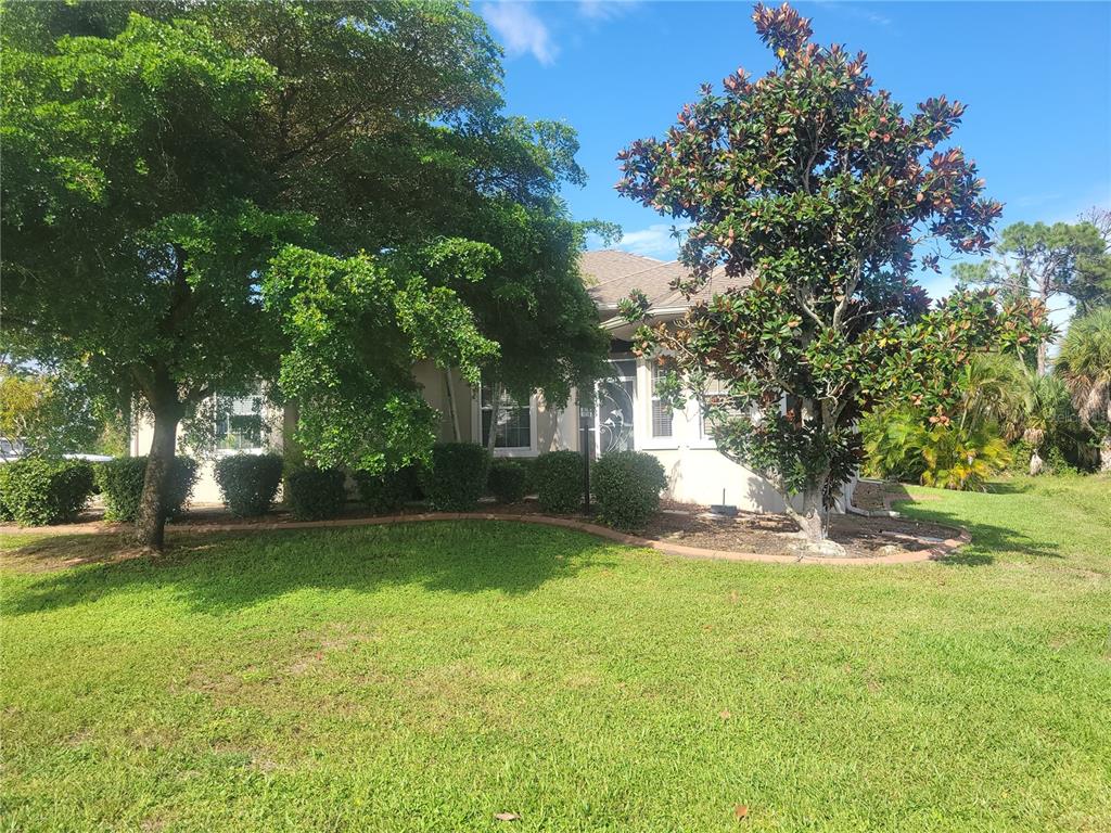 A single-story house with a lawn, mature trees, and a landscaped garden bed — 12 TEE VIEW COURT, ROTONDA WEST, FL
