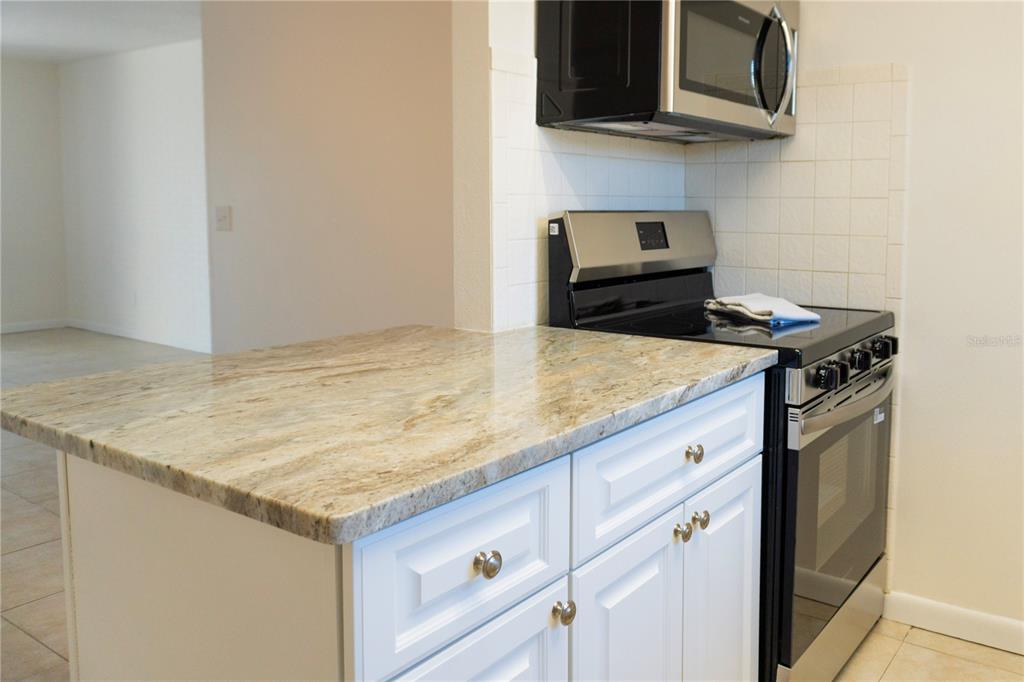 A kitchen features white cabinets, granite countertops, and a black stove with a microwave above — 4725 AVON COURT, ST CLOUD, FL