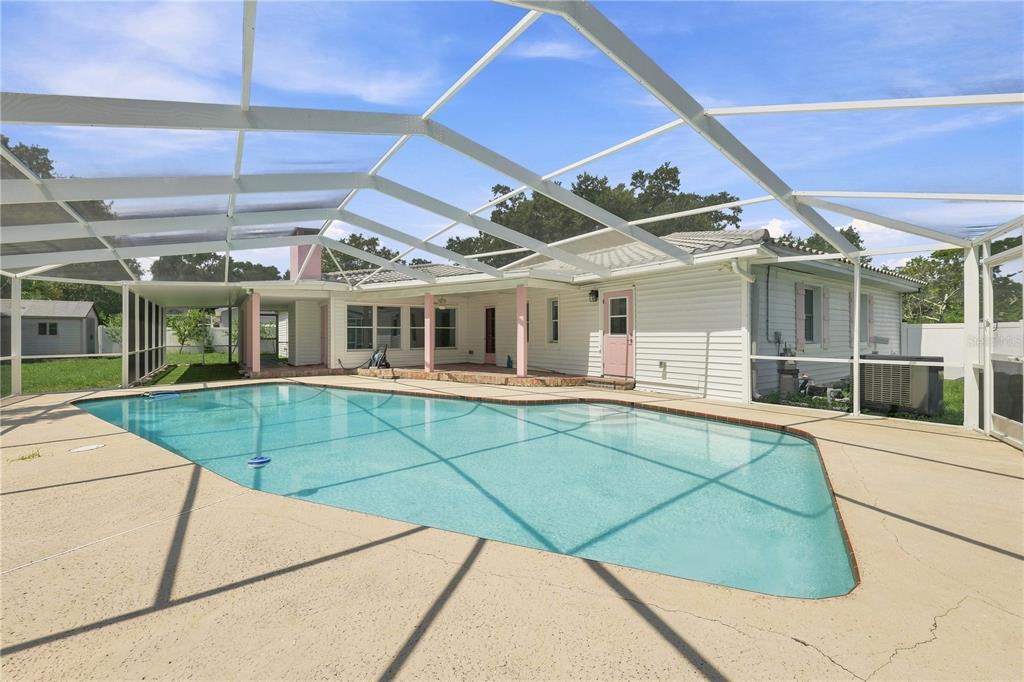 A swimming pool with a screened enclosure sits on a patio behind a white house — 1361 PINELLAS ROAD, CLEARWATER, FL
