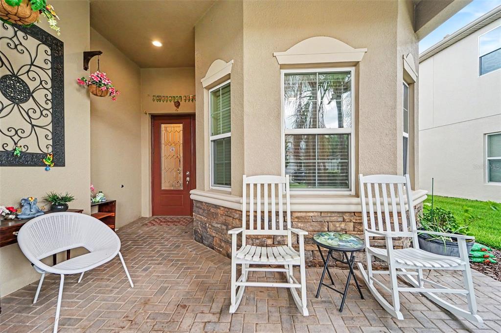 A covered front porch features brick pavers, two white rocking chairs, and a red door — 30867 LINDENTREE DRIVE, WESLEY CHAPEL, FL