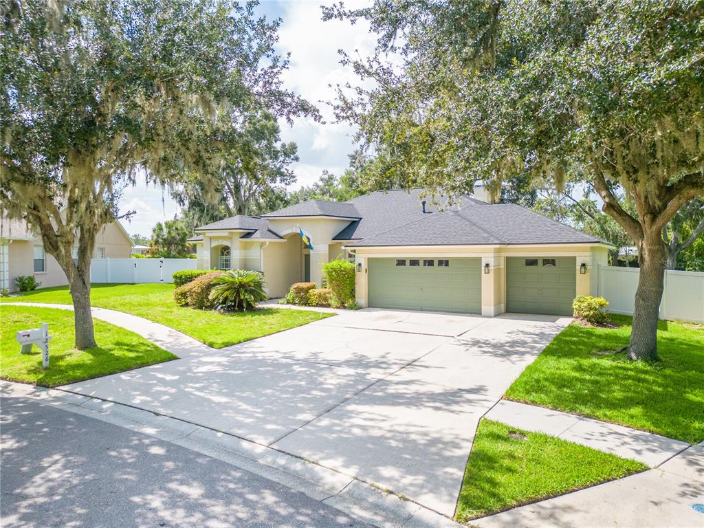 A single-story house with a three-car garage, light-colored stucco walls, and mature oak trees — 12526 RIVER BIRCH DRIVE, RIVERVIEW, FL