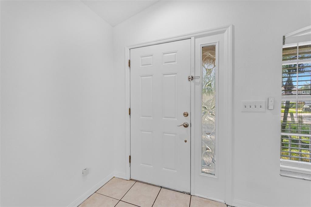 A white front door with a decorative glass sidelight in a tiled entryway — 6115 SAND KEY LANE, WESLEY CHAPEL, FL