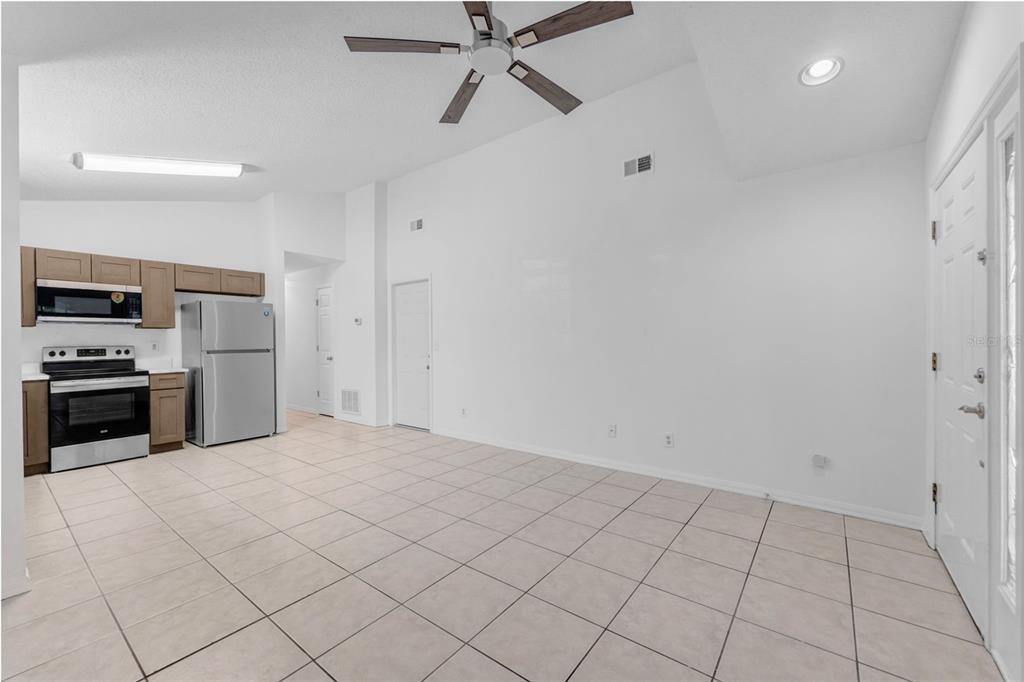 An open-concept kitchen and living area with tile flooring, white walls, and a ceiling fan — 6115 SAND KEY LANE, WESLEY CHAPEL, FL