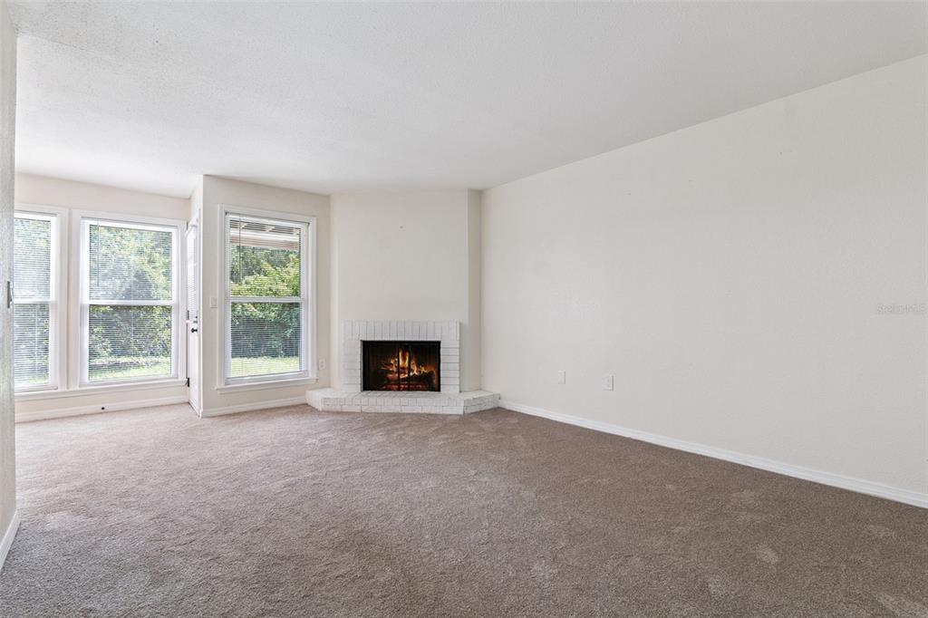A carpeted living room features a corner fireplace with a white brick surround and windows — 623 GRENADINE COURT UNIT 623, WINTER PARK, FL