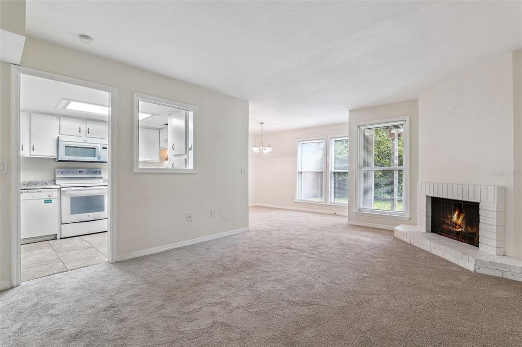 A living room with beige carpet, a white brick fireplace, and a view into the kitchen — 623 GRENADINE COURT UNIT 623, WINTER PARK, FL